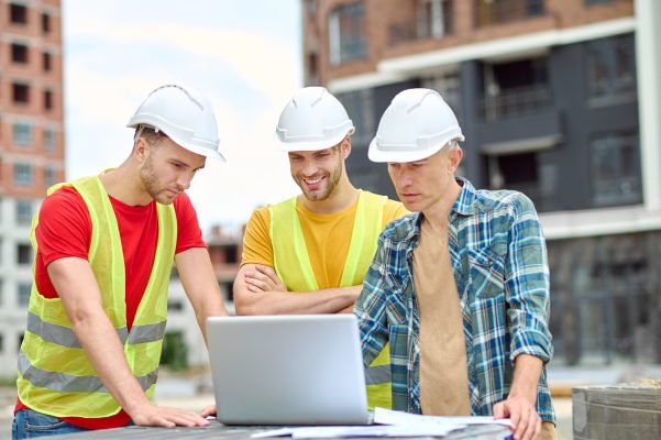 important-information-three-men-protective-helmet-looking-laptop-with-interest-while-standing-construction-site-day-min important-information-three-men-protective-helmet-looking-laptop-with-interest-while-standing-construction-site-day-min